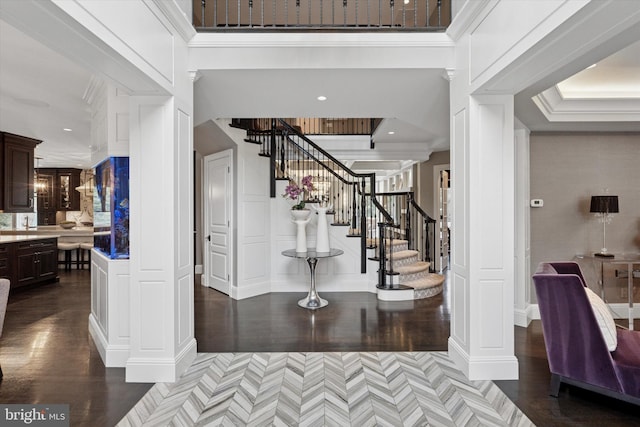 foyer with stairway, a decorative wall, ornate columns, and wood finished floors