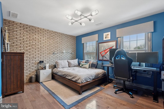 bedroom with hardwood / wood-style flooring, brick wall, and visible vents