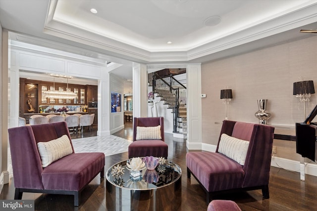 living area featuring a raised ceiling, ornate columns, wood finished floors, and stairs