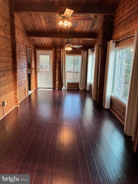 unfurnished living room featuring a ceiling fan, lofted ceiling with beams, wood walls, wood ceiling, and dark wood-style flooring
