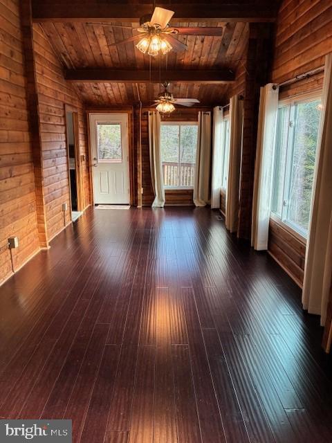 unfurnished living room featuring dark wood-type flooring, beamed ceiling, wood walls, and wooden ceiling