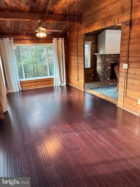 unfurnished living room featuring a brick fireplace, wood walls, lofted ceiling with beams, hardwood / wood-style floors, and a wealth of natural light
