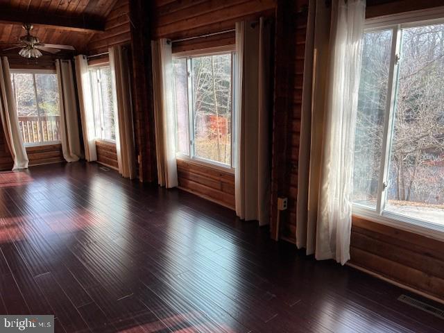 empty room featuring visible vents, vaulted ceiling with beams, dark wood-type flooring, wooden ceiling, and a ceiling fan