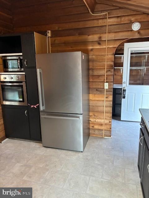 kitchen featuring wooden walls, stainless steel appliances, and lofted ceiling