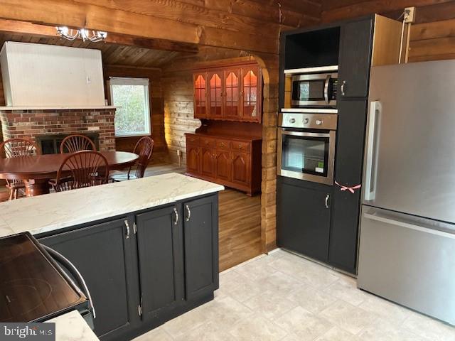 kitchen featuring vaulted ceiling with beams, a chandelier, wood walls, stainless steel appliances, and dark cabinets
