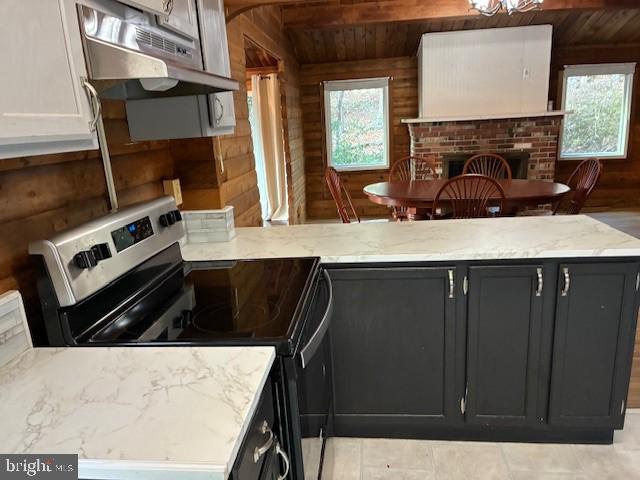 kitchen with stainless steel electric range oven, light stone counters, wood walls, and under cabinet range hood