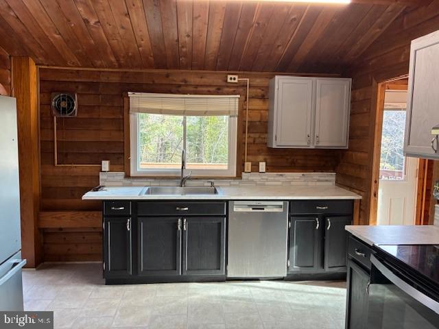 kitchen featuring a sink, wooden walls, appliances with stainless steel finishes, and wooden ceiling