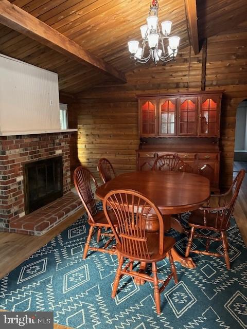 dining area with lofted ceiling with beams, a notable chandelier, wood finished floors, and wood walls