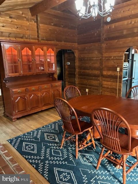 dining room featuring arched walkways, wooden walls, an inviting chandelier, and light wood finished floors