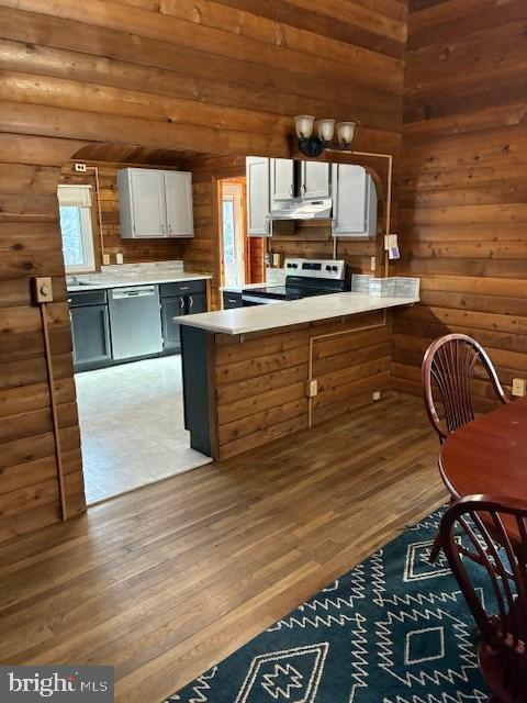 kitchen with wooden walls, wood finished floors, a peninsula, stainless steel appliances, and under cabinet range hood