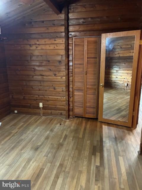 unfurnished bedroom featuring hardwood / wood-style flooring, wooden walls, and a closet