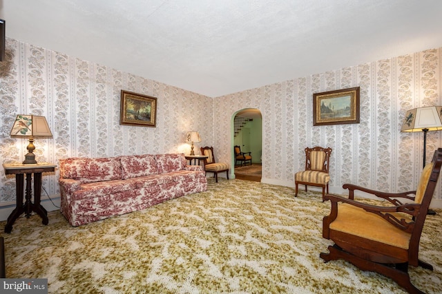 carpeted living room featuring arched walkways and wallpapered walls