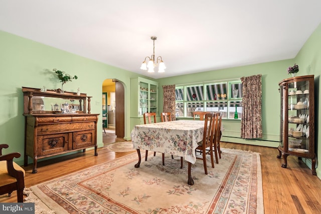 dining space featuring arched walkways, a baseboard heating unit, a chandelier, and wood finished floors