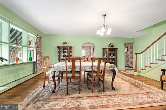 dining space with arched walkways, a chandelier, wood finished floors, a baseboard radiator, and stairway