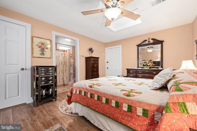bedroom featuring visible vents, wood finished floors, ceiling fan, connected bathroom, and a skylight