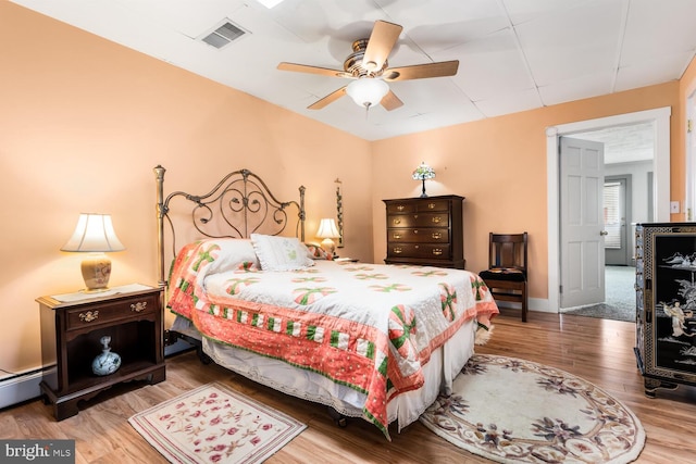 bedroom featuring visible vents, a baseboard heating unit, ceiling fan, and wood finished floors