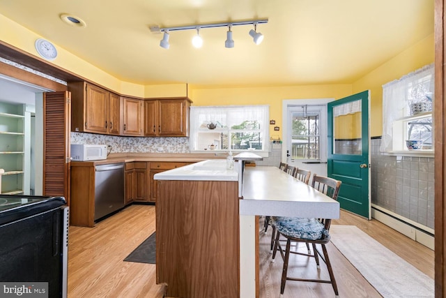 kitchen featuring a breakfast bar, white microwave, baseboard heating, light wood-type flooring, and stainless steel dishwasher