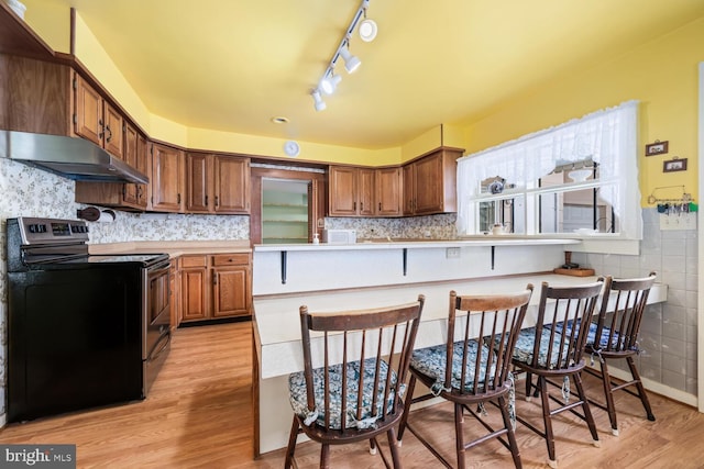 kitchen with light countertops, light wood-style floors, under cabinet range hood, and electric range