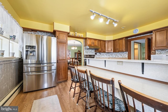 kitchen with a breakfast bar, white microwave, stainless steel fridge, light countertops, and a baseboard heating unit