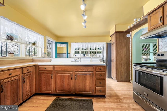 kitchen featuring brown cabinetry, under cabinet range hood, a sink, light wood-style flooring, and appliances with stainless steel finishes