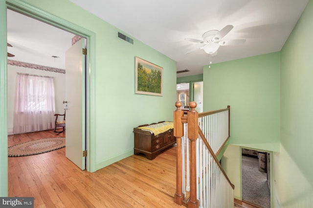 hallway with baseboards, visible vents, light wood-style flooring, and an upstairs landing