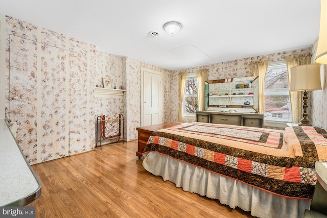 bedroom featuring multiple windows, wallpapered walls, and wood finished floors