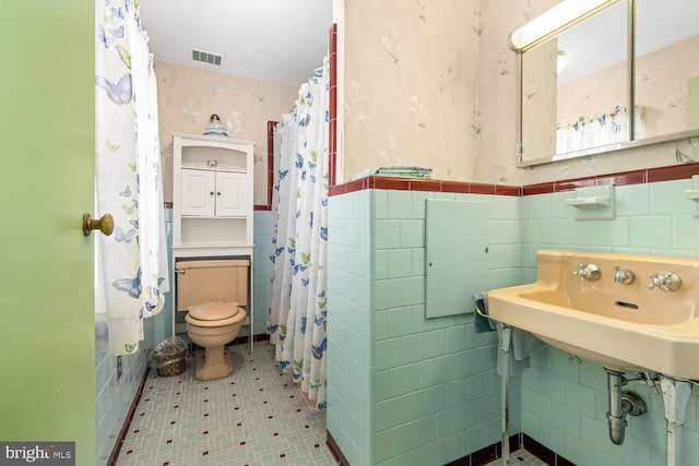 full bath with visible vents, wallpapered walls, a wainscoted wall, and tile walls