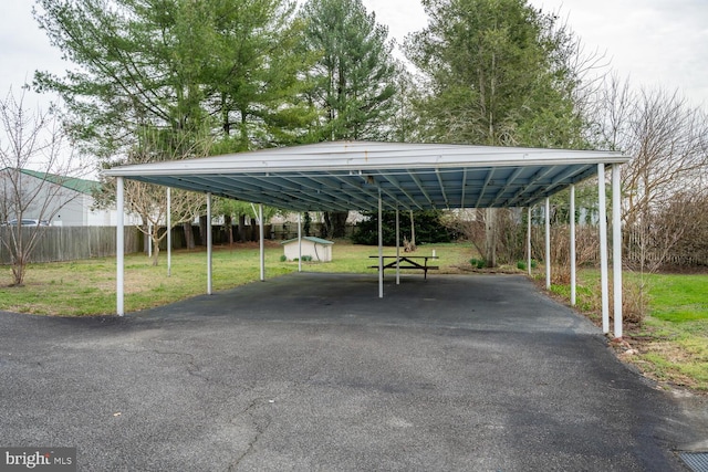 view of parking / parking lot featuring aphalt driveway, fence, and a carport