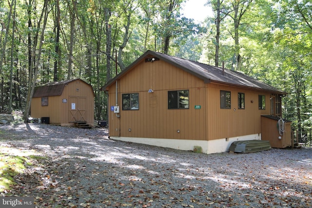 view of side of home featuring an outbuilding, entry steps, a forest view, and a storage shed