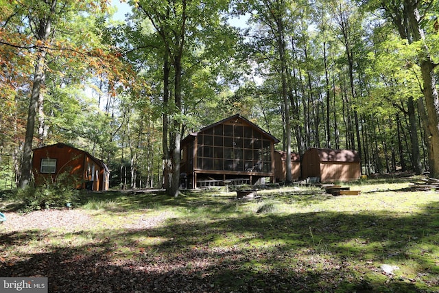 view of yard featuring an outbuilding, a shed, a forest view, and a sunroom
