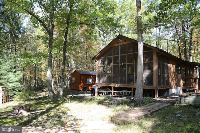 rear view of house with an outdoor structure, a wooded view, and a sunroom