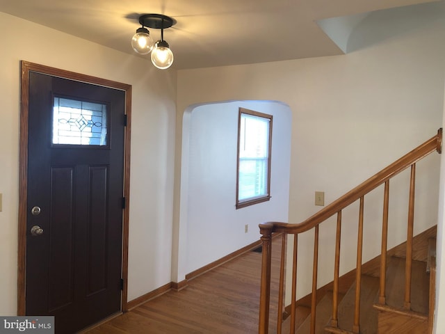 entrance foyer featuring wood finished floors, a healthy amount of sunlight, arched walkways, and baseboards