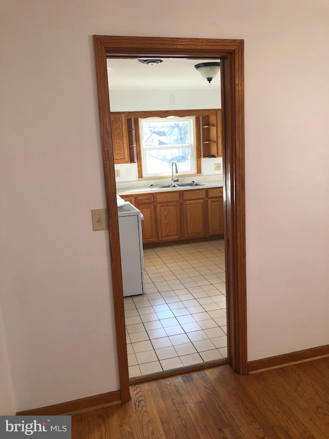 hall featuring a sink, light wood-type flooring, baseboards, and washer / clothes dryer