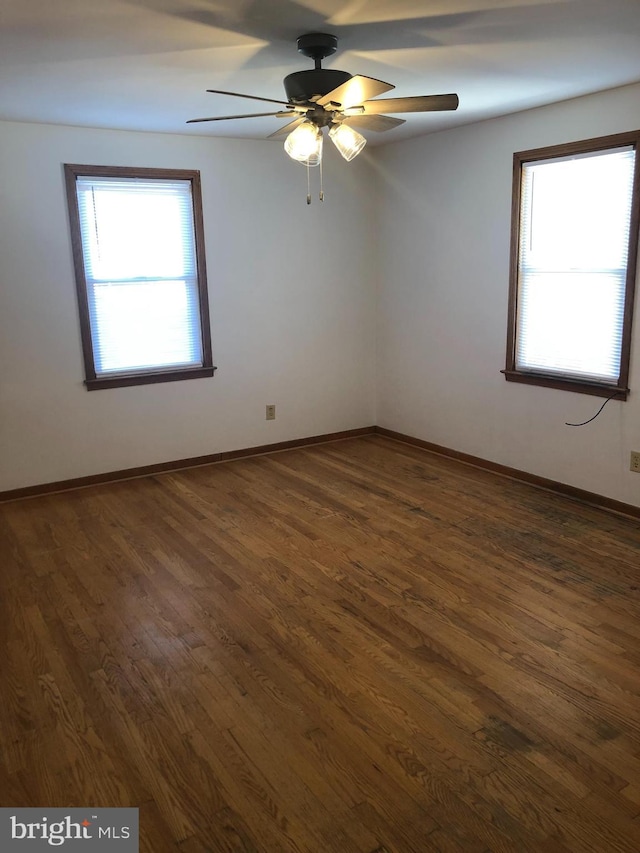 empty room with dark wood finished floors, a ceiling fan, and baseboards