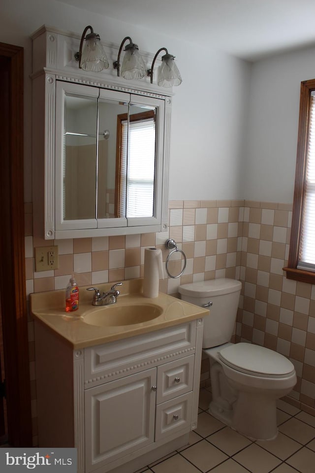 bathroom featuring vanity, a wainscoted wall, tile patterned floors, toilet, and tile walls