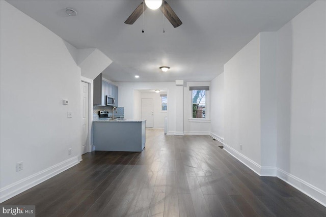 unfurnished living room featuring a sink, dark wood-type flooring, baseboards, and ceiling fan