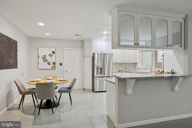 1220 Wendover Rd, Bryn Mawr, PA 19010 - kitchen featuring a peninsula, stainless steel fridge, a breakfast bar, decorative backsplash, and light stone counters
