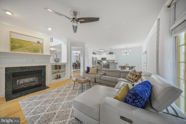 living area featuring wood finished floors, ceiling fan with notable chandelier, ornamental molding, recessed lighting, and a premium fireplace