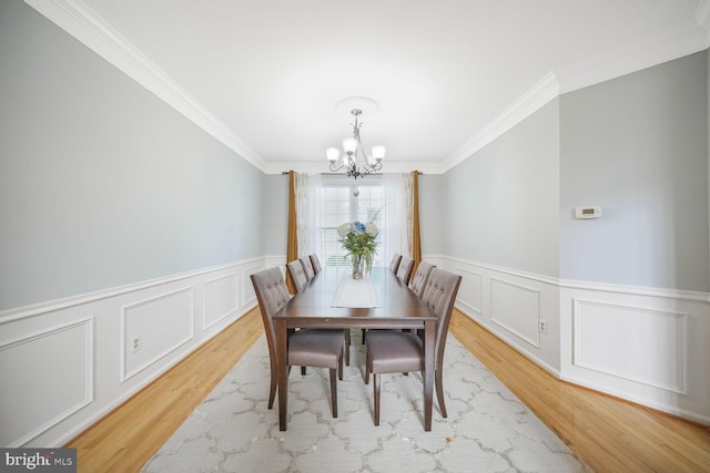 dining area with ornamental molding, light wood-style flooring, and a notable chandelier