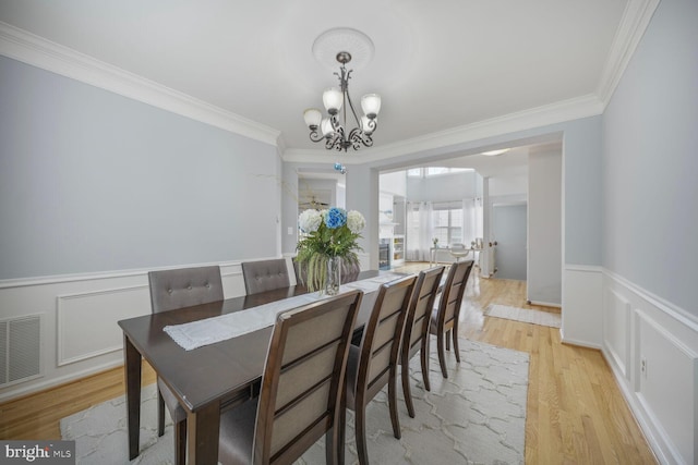 dining area featuring visible vents, crown molding, a notable chandelier, and light wood-type flooring