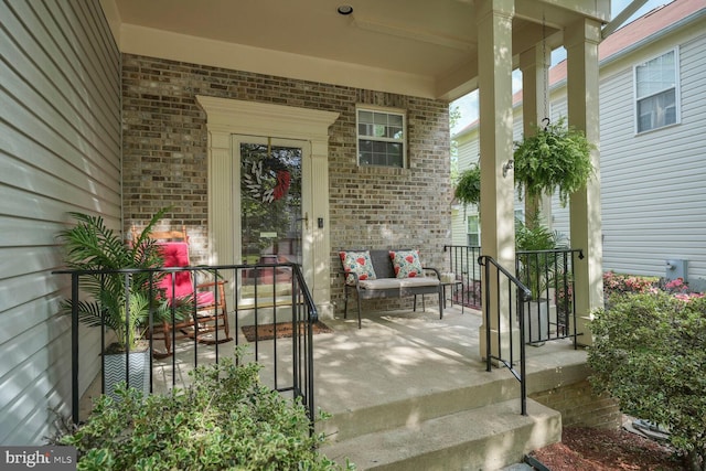 view of exterior entry with brick siding and covered porch