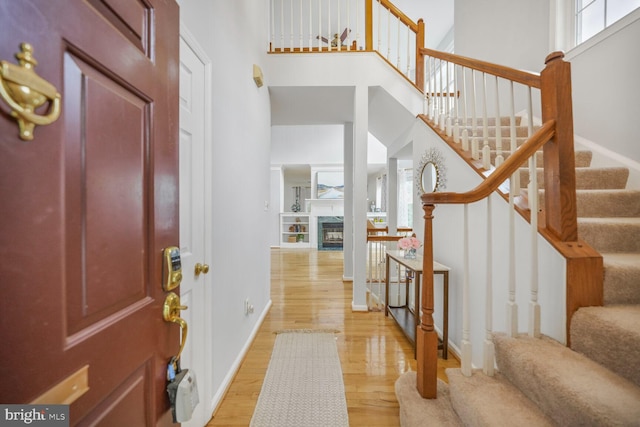 entryway with a fireplace, stairway, baseboards, a high ceiling, and light wood-style flooring