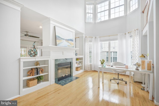 home office featuring ceiling fan, a fireplace, plenty of natural light, wood finished floors, and a towering ceiling