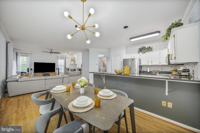 dining space featuring ornamental molding, light wood-style flooring, and ceiling fan with notable chandelier