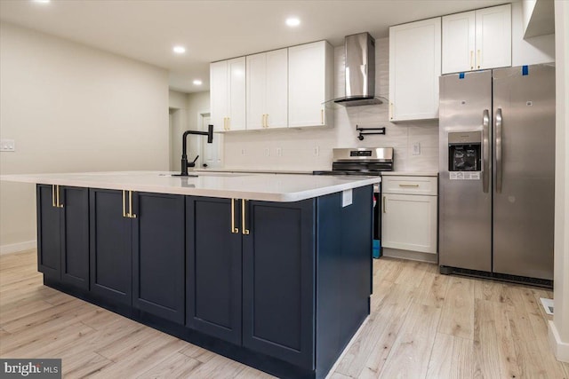 kitchen featuring wall chimney exhaust hood, light wood finished floors, white cabinets, and stainless steel appliances