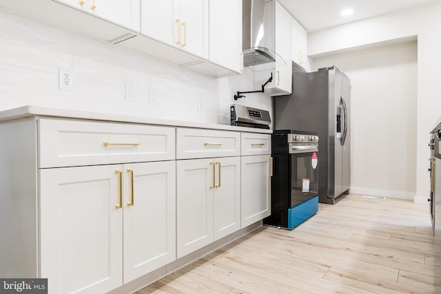 kitchen featuring wall chimney range hood, appliances with stainless steel finishes, light wood-style floors, light countertops, and white cabinetry