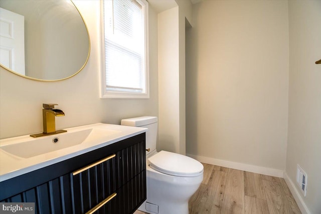 half bath with a healthy amount of sunlight, toilet, wood finished floors, and visible vents