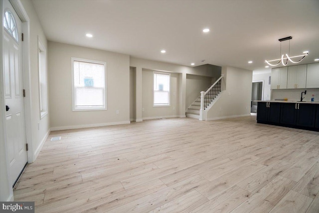 unfurnished living room with stairs, baseboards, recessed lighting, light wood finished floors, and a notable chandelier