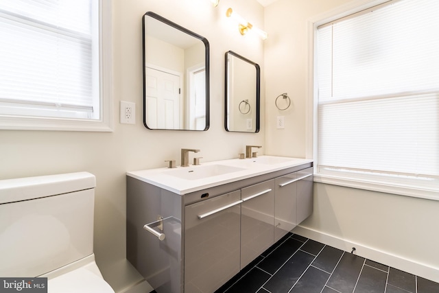 bathroom featuring double vanity, a sink, tile patterned floors, baseboards, and toilet