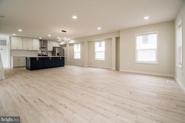 unfurnished living room featuring recessed lighting, baseboards, light wood finished floors, and a notable chandelier